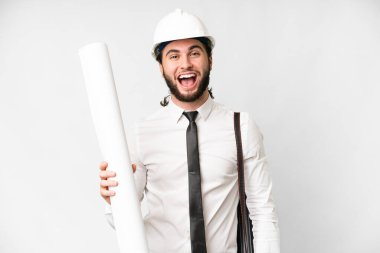 Young architect man with helmet and holding blueprints over isolated white background with surprise facial expression
