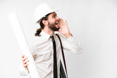Young architect man with helmet and holding blueprints over isolated white background shouting with mouth wide open to the side