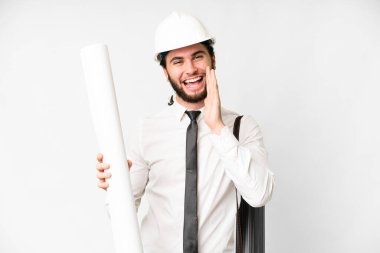Young architect man with helmet and holding blueprints over isolated white background shouting with mouth wide open