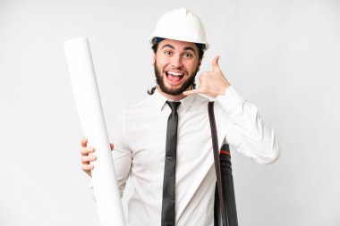 Young architect man with helmet and holding blueprints over isolated white background making phone gesture. Call me back sign