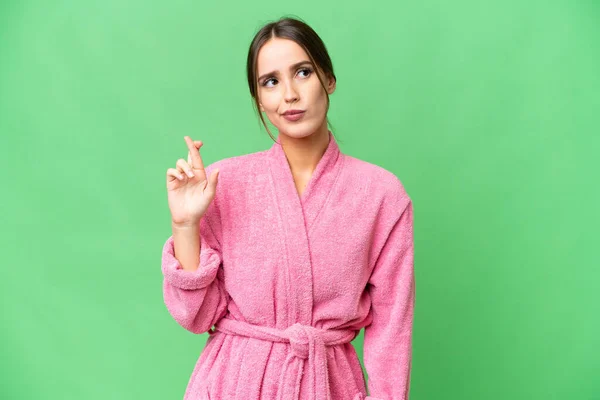 Young beautiful woman in a bathrobe over isolated chroma key background with fingers crossing and wishing the best