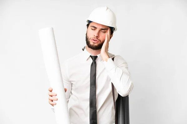 Young architect man with helmet and holding blueprints over isolated white background with headache
