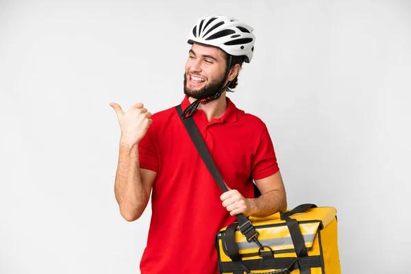Young delivery man with thermal backpack over isolated white background pointing to the side to present a product