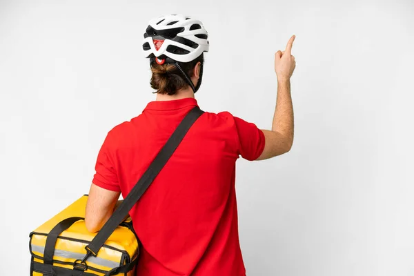 Young delivery man with thermal backpack over isolated white background pointing back with the index finger