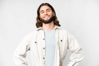 Soyutlanmış beyaz arka planda genç yakışıklı adam kolları kalçasında ve gülümsüyor.