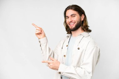 İzole edilmiş beyaz arka planda genç yakışıklı bir adam parmağını yana uzatıyor ve bir ürün sunuyor.