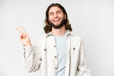 Genç yakışıklı adam izole edilmiş beyaz arka planda gülümsüyor ve zafer işareti gösteriyor.