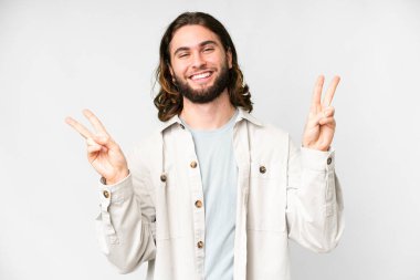 İzole edilmiş beyaz arka planda genç yakışıklı adam iki eliyle zafer işareti gösteriyor.