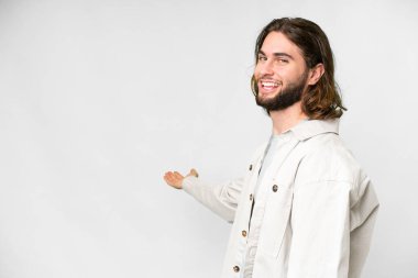İzole edilmiş beyaz arka planda genç yakışıklı adam davet edilmek için ellerini yana uzatıyor.