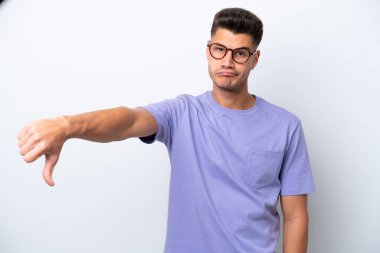 Beyaz arka planda izole genç beyaz adam olumsuz ifade ile baş parmağını göstermektedir