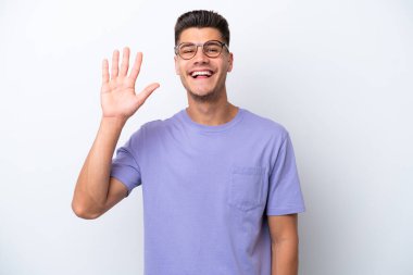 Beyaz arka planda izole edilmiş genç beyaz bir adam mutlu bir ifadeyle selamlıyor.