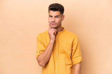 Young caucasian man isolated on beige background and thinking
