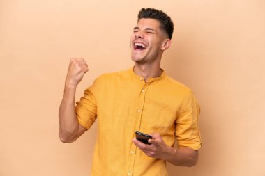 Beyazlı genç adam bej arka planda izole edilmiş ve telefon zafer pozisyonunda.