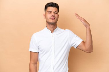 Beyazlı genç bir adam bej arka planda izole edilmiş, yorgun ve hasta bir ifadeyle.