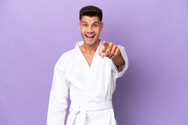 Mor arka planda karate yapan genç beyaz adam şaşırmış ve ön tarafı işaret ediyor.