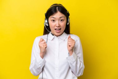 Telemarketer Chinese woman working with a headset isolated on yellow background celebrating a victory in winner position