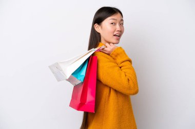 Beyaz arka planda izole edilmiş genç bir Çinli kadın alışveriş torbaları tutuyor ve gülümsüyor.