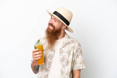 Redhead man with long beard drinking a cocktail on a beach isolated on white background looking to the side and smiling