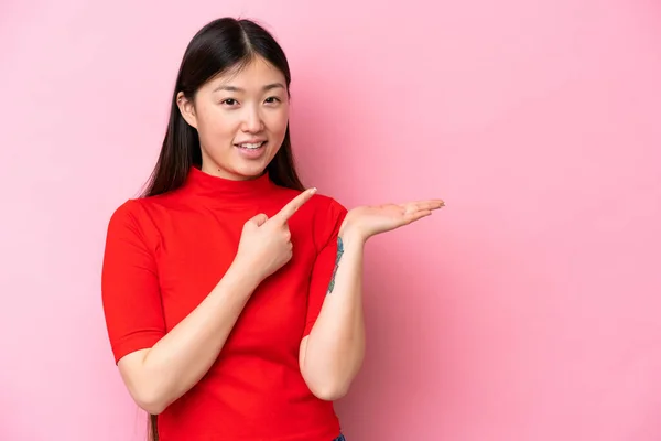 Young Chinese woman isolated on pink background holding copyspace imaginary on the palm to insert an ad