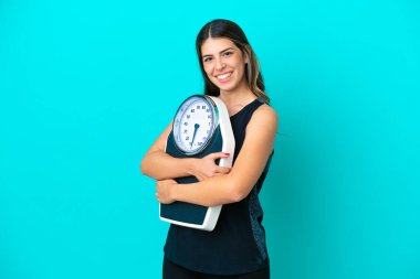 Genç İtalyan kadın, mavi arka planda tartı makinesiyle izole edilmiş.