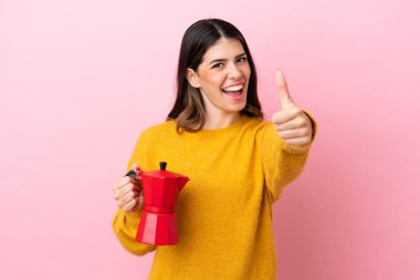Young Italian woman holding a coffee maker isolated on pink background with thumbs up because something good has happened