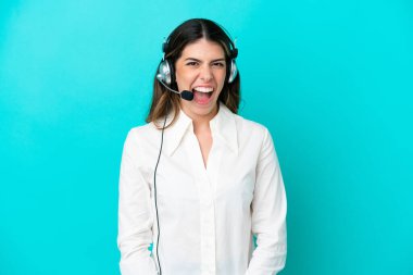 Tele pazarlamacı İtalyan kadın kulaklıkla çalışıyor mavi arka planda, şaşırmış bir yüz ifadesi var.