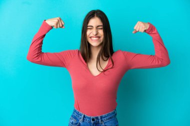 Mavi arka planda izole edilmiş beyaz bir kadın güçlü bir jest yapıyor.