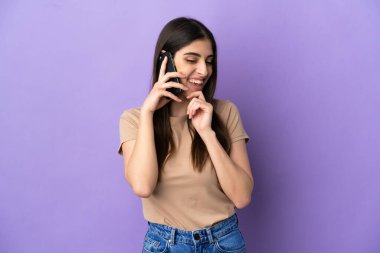 Mor arka planda izole edilmiş cep telefonu kullanan beyaz bir kadın yana bakıyor ve gülümsüyor.