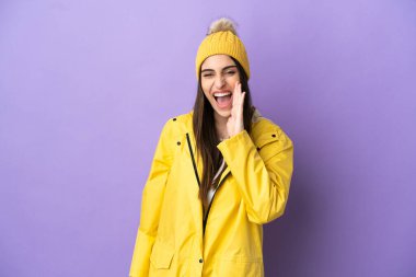 Young caucasian woman wearing a rainproof coat isolated on purple background shouting with mouth wide open