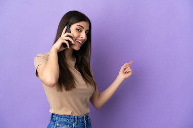 Young caucasian woman using mobile phone isolated on purple background pointing back
