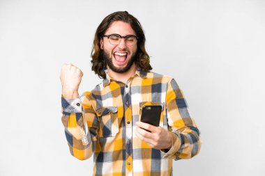 Galibiyet pozisyonunda telefonuyla izole edilmiş beyaz arka planda genç yakışıklı bir adam.