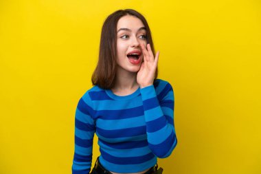 Young Ukrainian woman isolated on yellow background shouting with mouth wide open to the side