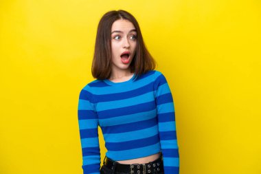 Young Ukrainian woman isolated on yellow background doing surprise gesture while looking to the side