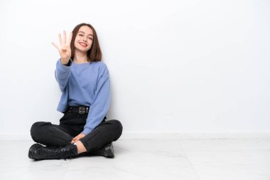Young Ukrainian woman sitting on the floor isolated on white background happy and counting four with fingers