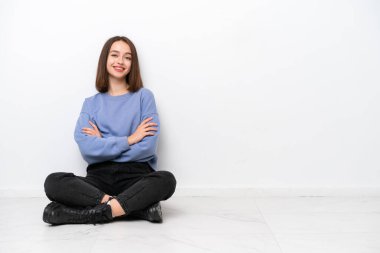 Genç Ukraynalı kadın, beyaz arka planda izole bir şekilde yerde oturuyor ve kollarını ön cephede kavuşturuyor.