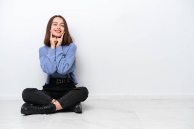 Young Ukrainian woman sitting on the floor isolated on white background smiling with a happy and pleasant expression