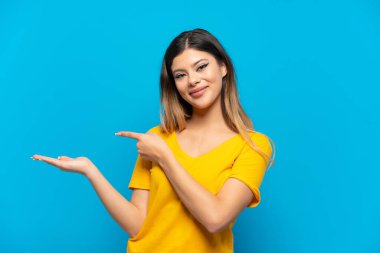 Young Russian girl isolated on blue background holding copyspace imaginary on the palm to insert an ad