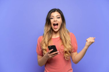 Genç Rus kız mavi arka planda cep telefonu kullanarak ve zafer jesti yaparak izole edildi.