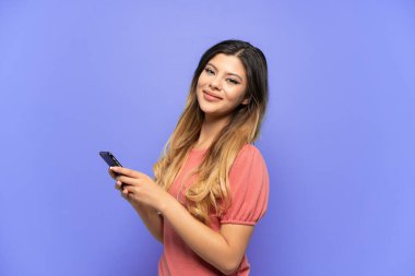 Genç Rus kız mavi arka planda izole edilmiş. Cep telefonuyla mesaj ya da e-posta gönderiyor.
