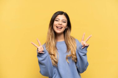 Young Russian girl isolated on yellow background smiling and showing victory sign
