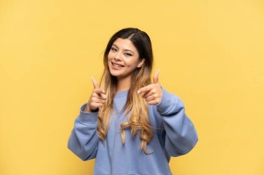 Young Russian girl isolated on yellow background pointing to the front and smiling
