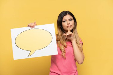 Young Russian girl isolated on yellow background holding a placard with speech bubble icon doing silence gesture