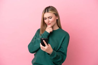 Genç beyaz kadın pembe arka planda izole edilmiş düşünüyor ve bir mesaj gönderiyor.