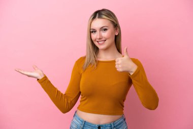 Beyaz, pembe arka planda izole edilmiş genç bir kadın. Avucunun içinde hayali bir şey tutuyor. Bir ilan vermek için.