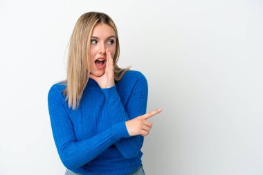 Beyaz arka planda izole edilmiş genç beyaz bir kadın bir ürünü sunmak ve bir şeyler fısıldamak için kenarı işaret ediyor.