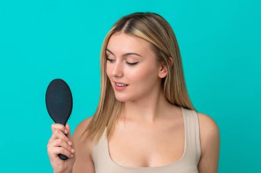 Genç beyaz kadın mavi arka planda saç tarağıyla izole edilmiş ve ona bakıyor.