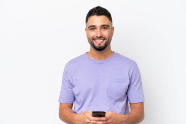 Genç Arap yakışıklı adam beyaz arka planda izole edilmiş cep telefonuyla bir mesaj gönderiyor.