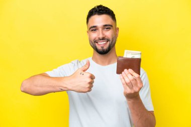 Young Arab man holding a wallet isolated on yellow background with thumbs up because something good has happened
