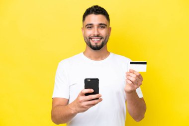 Young Arab handsome man isolated on yellow background buying with the mobile with a credit card