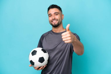 Young Arab handsome man isolated on blue background with soccer ball and with thumb up